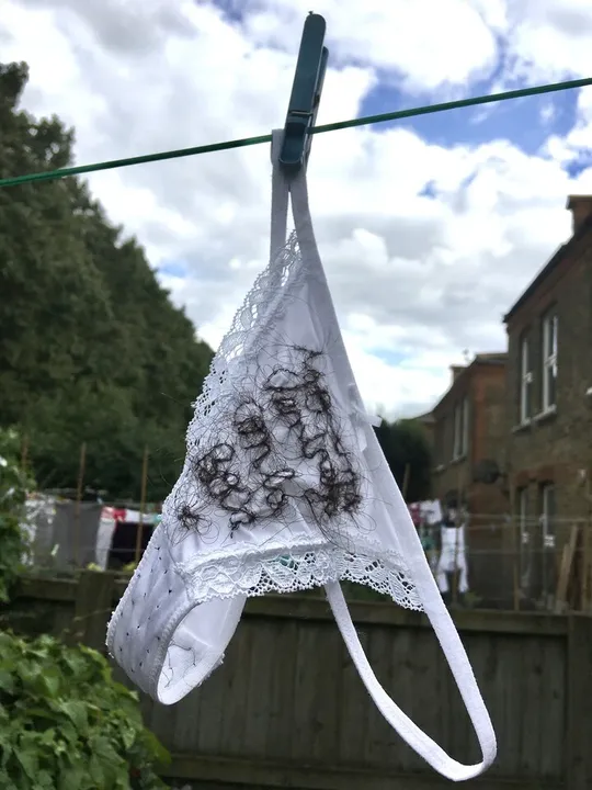 White panties embroidered with human hair lying on the rope in the garden. Belonging to the work My desire is a ghost.